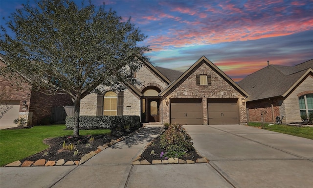 french provincial home featuring brick siding, an attached garage, concrete driveway, and a yard