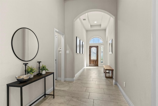 entryway featuring arched walkways, a high ceiling, baseboards, and light tile patterned flooring