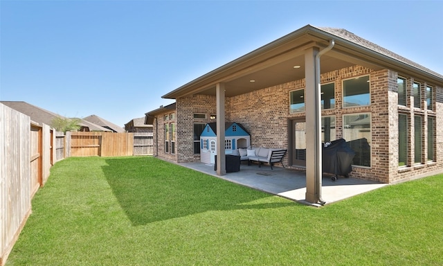 rear view of house with brick siding, a fenced backyard, a lawn, and a patio area