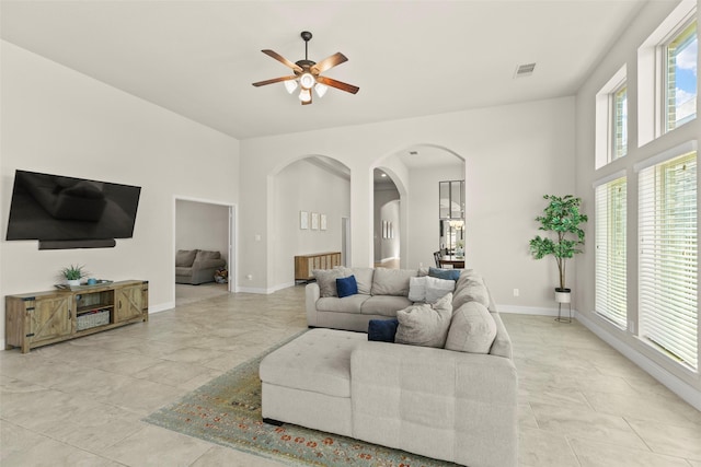 living room featuring visible vents, baseboards, a high ceiling, arched walkways, and a ceiling fan