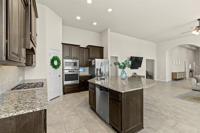 kitchen featuring backsplash, open floor plan, stainless steel appliances, arched walkways, and dark brown cabinets