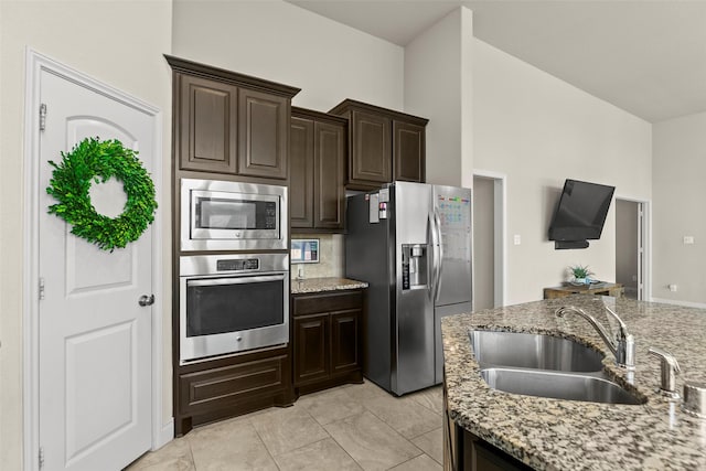 kitchen with a sink, light stone counters, dark brown cabinetry, appliances with stainless steel finishes, and light tile patterned floors