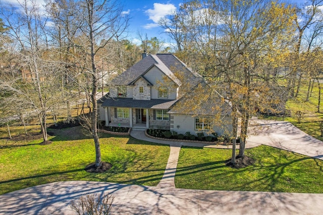 french country inspired facade with a front yard, covered porch, a shingled roof, concrete driveway, and stone siding