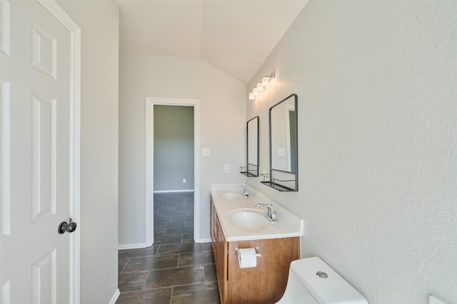 bathroom with a sink, toilet, double vanity, and vaulted ceiling