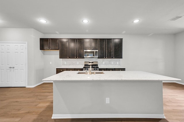 kitchen with a sink, decorative backsplash, appliances with stainless steel finishes, and light wood finished floors