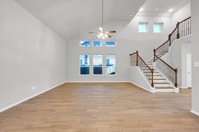 unfurnished living room featuring stairs, a towering ceiling, baseboards, and light wood finished floors