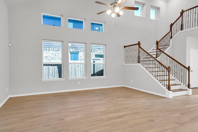 unfurnished living room with stairs, baseboards, light wood-style flooring, and a ceiling fan