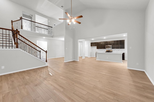 unfurnished living room featuring visible vents, baseboards, stairs, light wood-style flooring, and a ceiling fan