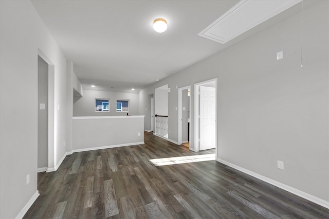 unfurnished living room featuring baseboards, dark wood-type flooring, and attic access