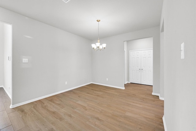 empty room featuring baseboards, light wood-type flooring, and a chandelier