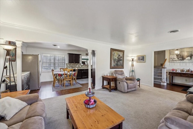 living room featuring visible vents, arched walkways, ornamental molding, stairs, and dark carpet