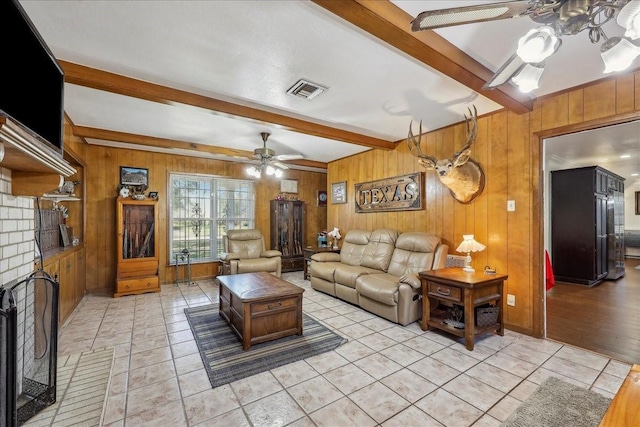 living room featuring visible vents, beamed ceiling, wood walls, a fireplace, and a ceiling fan