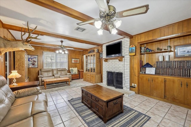 living room with wooden walls, a ceiling fan, visible vents, a fireplace, and beamed ceiling