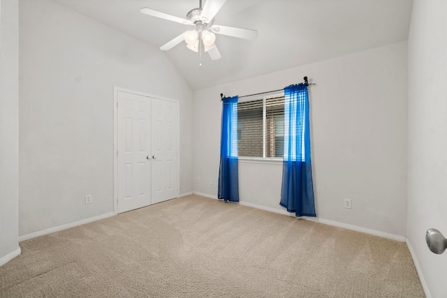 unfurnished bedroom featuring baseboards, lofted ceiling, light carpet, a closet, and a ceiling fan