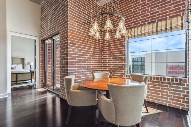 dining room featuring a high ceiling, an inviting chandelier, brick wall, and hardwood / wood-style flooring