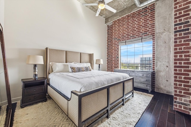 bedroom featuring wood-type flooring, a towering ceiling, brick wall, and ceiling fan
