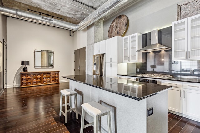 kitchen featuring dark countertops, appliances with stainless steel finishes, wall chimney exhaust hood, and a towering ceiling