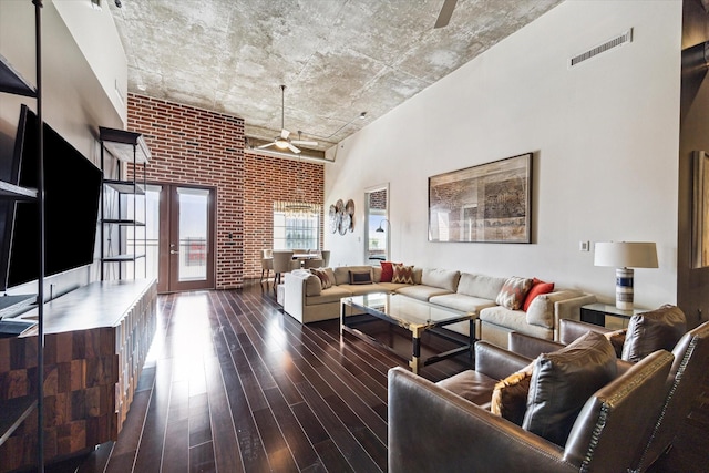 living room featuring ceiling fan, a high ceiling, brick wall, dark wood-type flooring, and visible vents