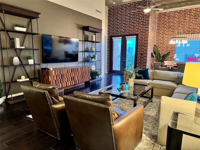 living room with brick wall, visible vents, a towering ceiling, a notable chandelier, and hardwood / wood-style floors