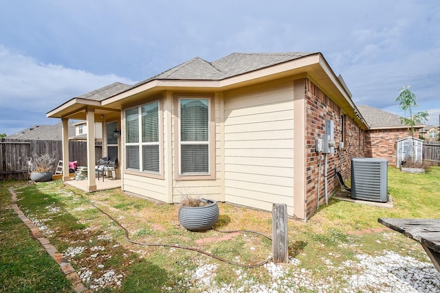 back of property featuring a lawn, central AC, fence, a shingled roof, and brick siding