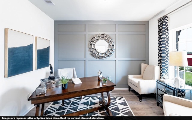 office featuring a decorative wall, light wood-type flooring, and visible vents