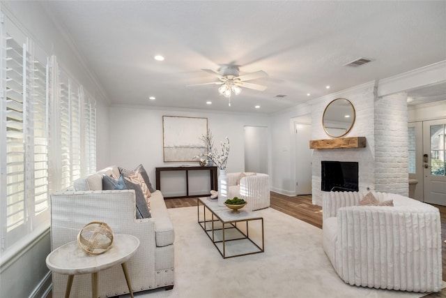 living area featuring crown molding, a brick fireplace, wood finished floors, and visible vents