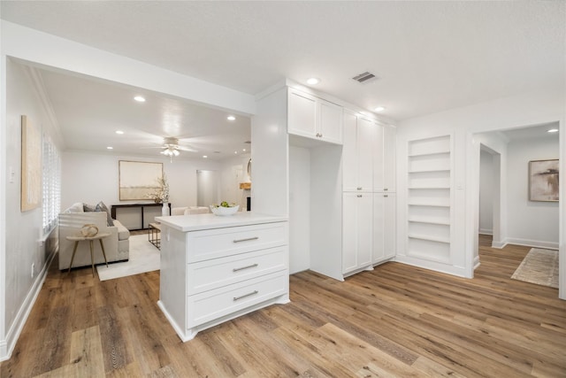 interior space with built in shelves, visible vents, light wood finished floors, white cabinetry, and open floor plan