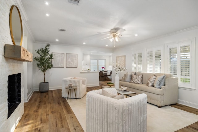 living room featuring ornamental molding, wood finished floors, a large fireplace, baseboards, and ceiling fan