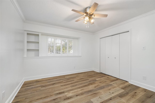 unfurnished bedroom featuring ornamental molding, a ceiling fan, wood finished floors, a closet, and baseboards