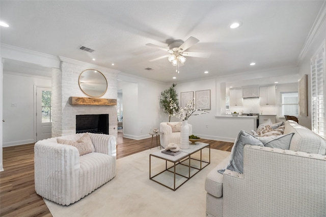 living room with visible vents, wood finished floors, a fireplace, and ornamental molding