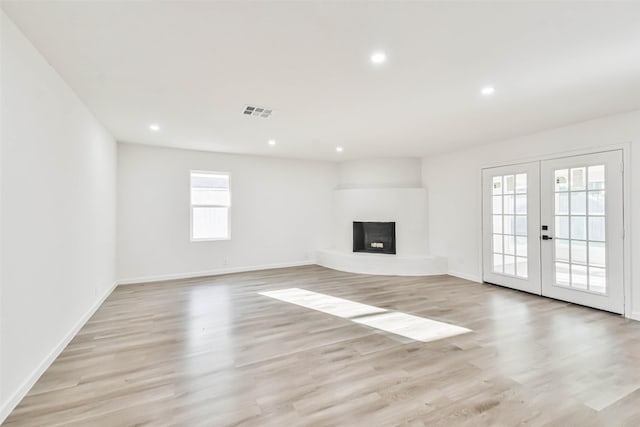 unfurnished living room with light wood-style flooring, french doors, visible vents, and a fireplace with raised hearth