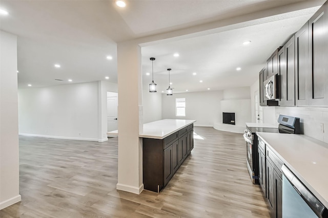 kitchen with light wood finished floors, open floor plan, appliances with stainless steel finishes, and a large fireplace