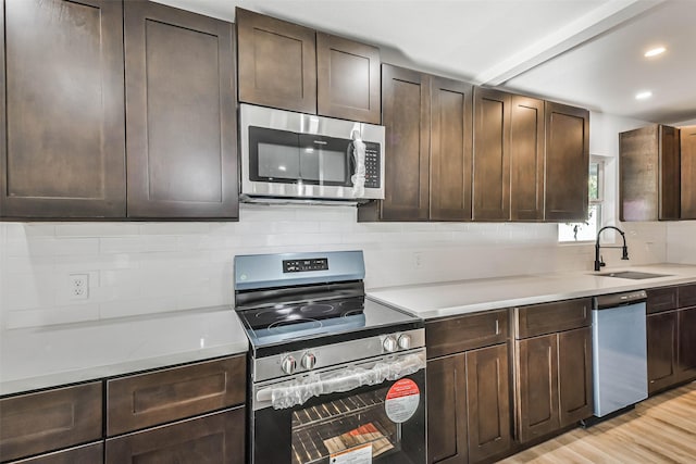 kitchen featuring light wood finished floors, backsplash, light countertops, stainless steel appliances, and a sink