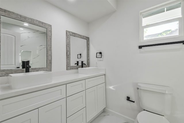 full bathroom with double vanity, toilet, marble finish floor, and a sink