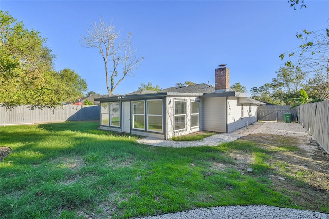 back of property with a yard, a fenced backyard, a chimney, and a sunroom