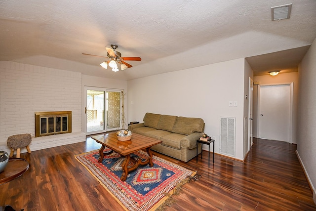 living room featuring visible vents, a brick fireplace, a textured ceiling, and wood finished floors