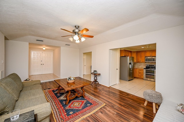 living area with light wood finished floors, visible vents, a textured ceiling, and ceiling fan