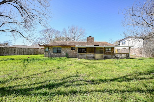 rear view of property featuring brick siding, fence, a lawn, and a chimney