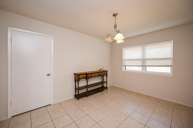 empty room with an inviting chandelier, light tile patterned floors, and baseboards