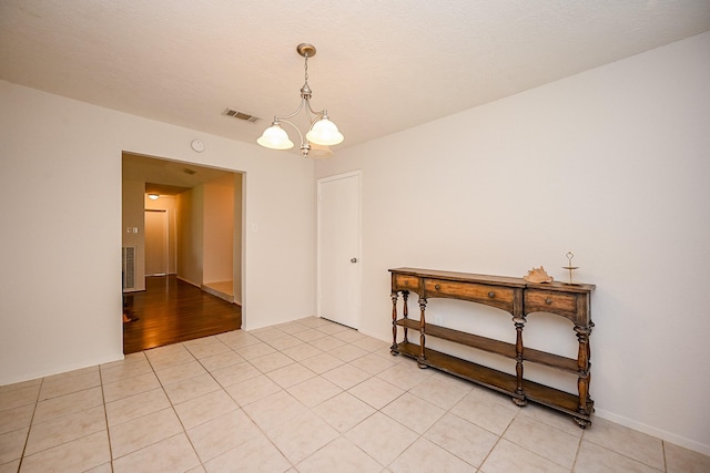 empty room featuring a textured ceiling, light tile patterned floors, visible vents, and a chandelier