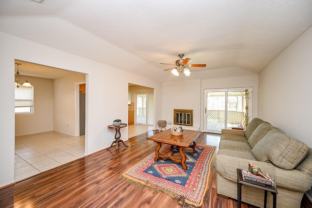 living area featuring ceiling fan with notable chandelier, a brick fireplace, wood finished floors, and a wealth of natural light