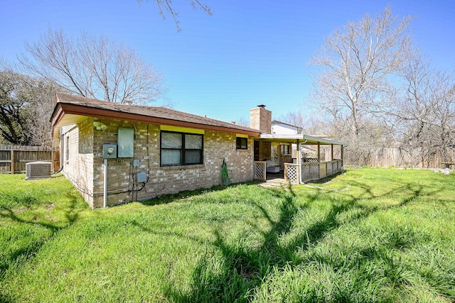 rear view of property featuring central air condition unit, a yard, a chimney, and fence