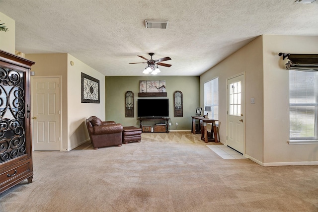 carpeted living room with a textured ceiling, baseboards, visible vents, and ceiling fan