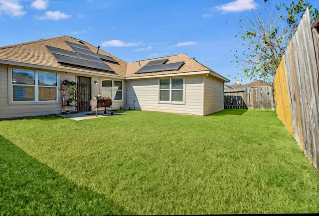 rear view of house with a patio, a lawn, a fenced backyard, and roof mounted solar panels