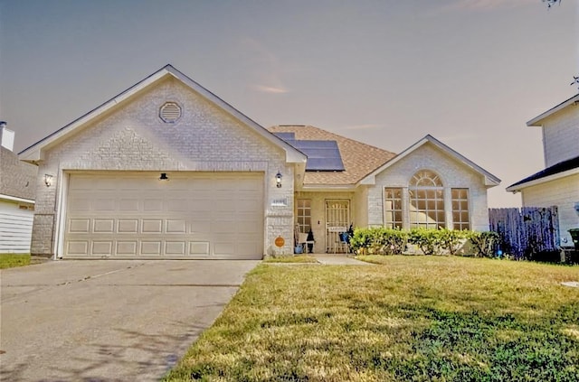 ranch-style house with brick siding, solar panels, an attached garage, a front yard, and driveway