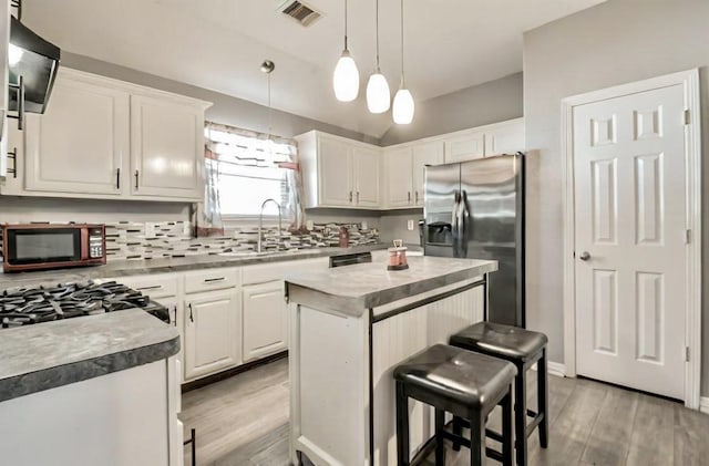 kitchen with visible vents, a kitchen island, a sink, stainless steel appliances, and white cabinets