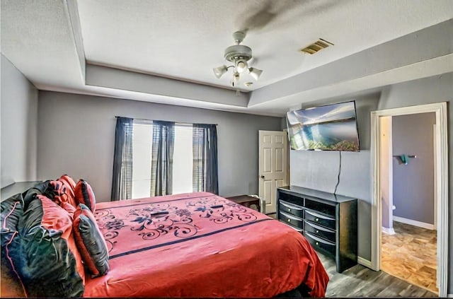 bedroom with visible vents, baseboards, wood finished floors, a raised ceiling, and a ceiling fan