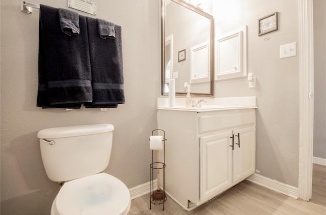 half bath with toilet, vanity, baseboards, and wood finished floors