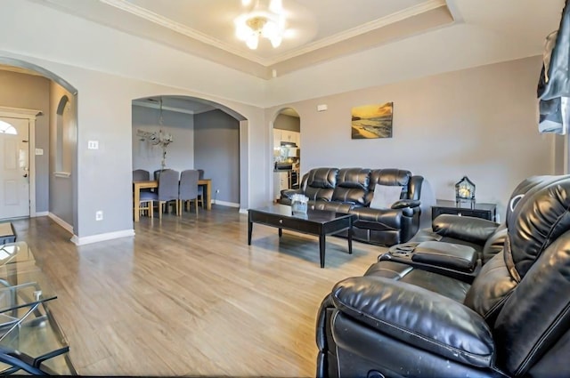 living area with a tray ceiling, wood finished floors, arched walkways, and ornamental molding