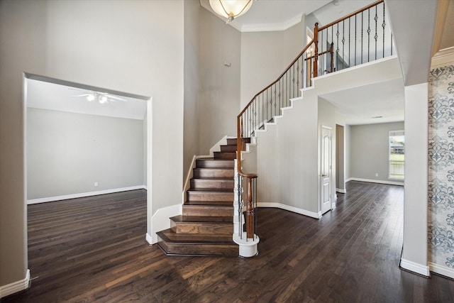 foyer featuring dark wood-style flooring, ceiling fan, baseboards, a towering ceiling, and stairs